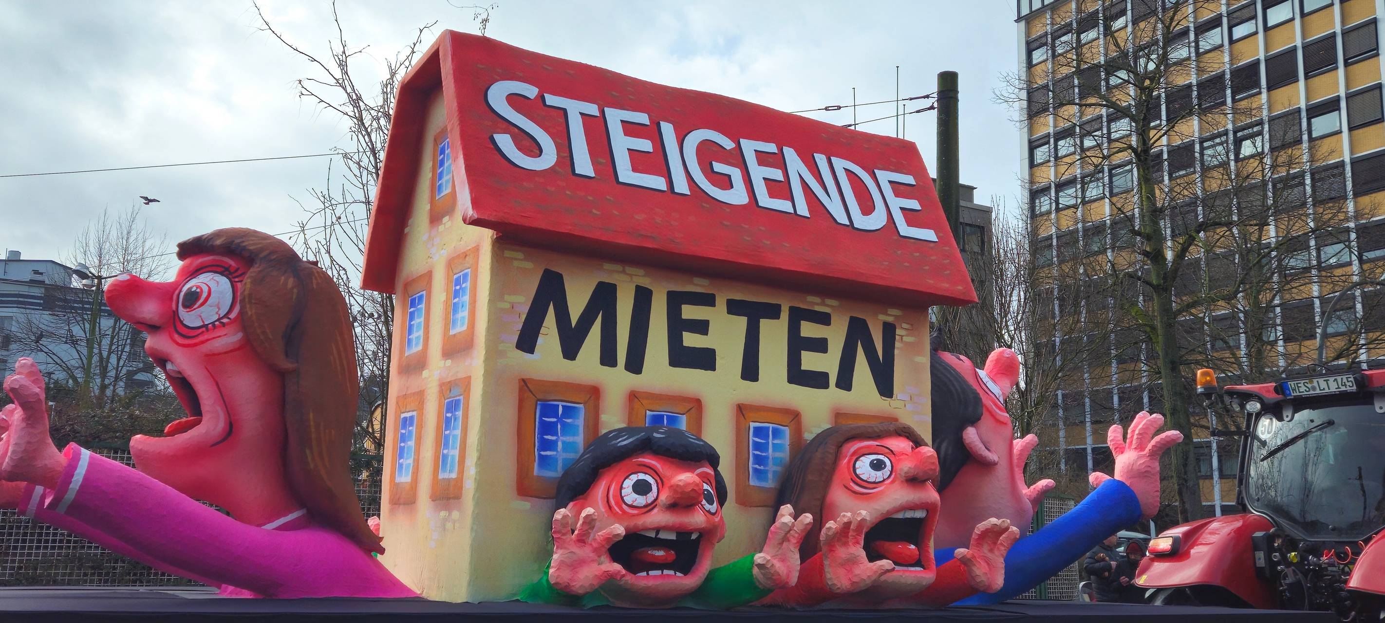 Mottowagen: Ein Haus steht auf Menschen, die von steigenden Mieten zerquetscht werden.