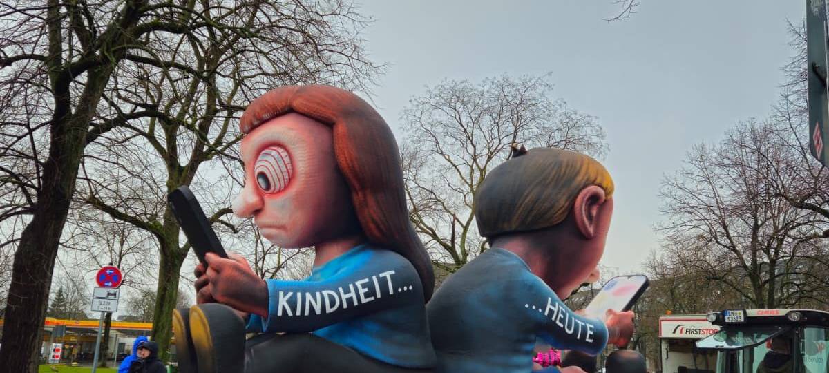 Zwei Kinderfiguren sitzen Rücken an Rücken nebeneinander und schauen ausschließlich auf ihre großen Handys.