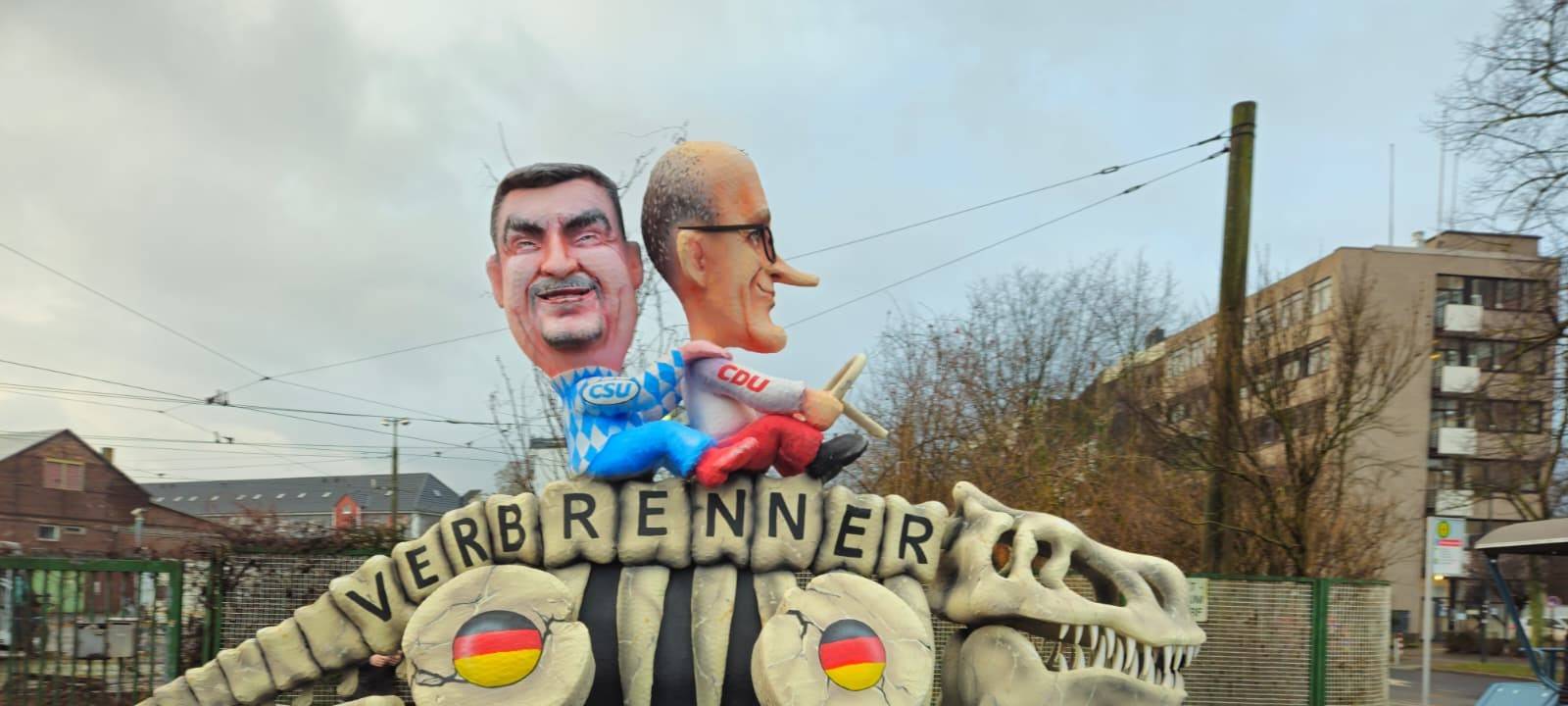 Die Figuren von Merz und Söder reiten auf einem klapprigen Dinosaurier, der die Verbrenner-Autos symbolisiert.