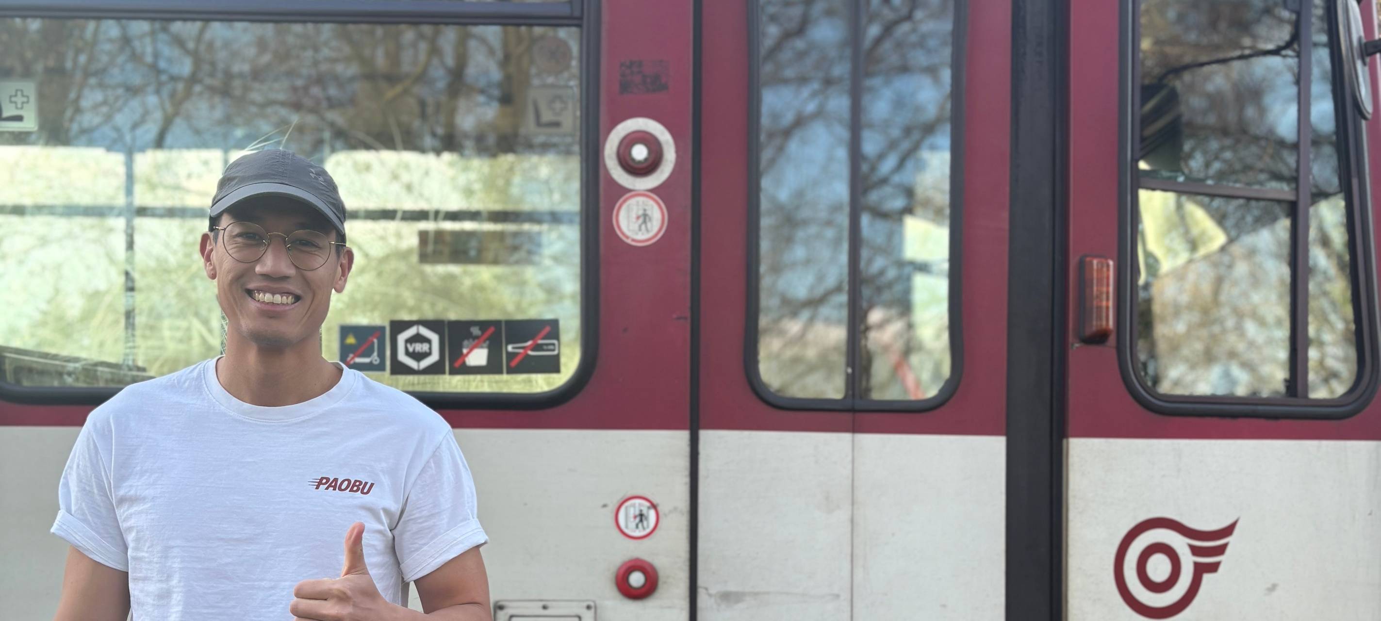 Oskar Cheong steht vor einer rot-weißen U-Bahn der Rheinbahn