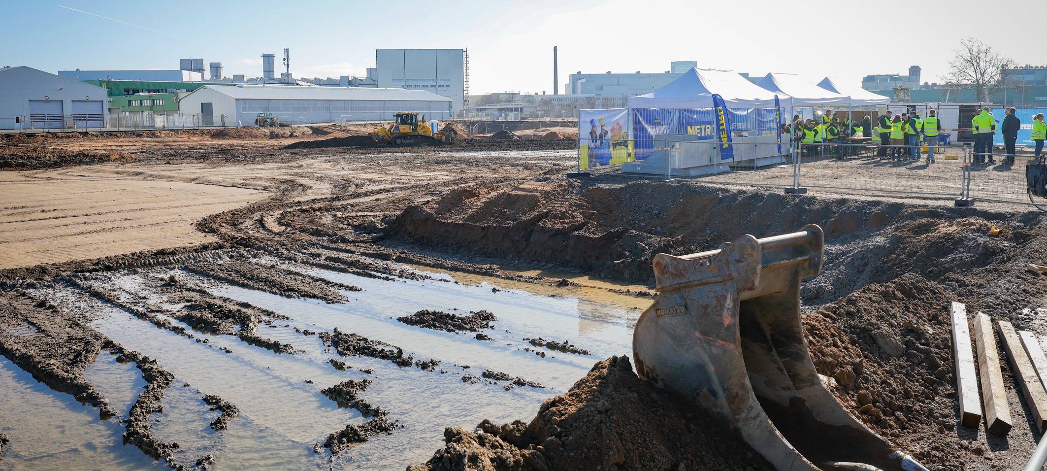 Große METRO-Baustelle an der Ulmenstraße mit Baggern und anderen schweren Geräten. Im Hintergrund weitere Hallen und ein Schornstein.