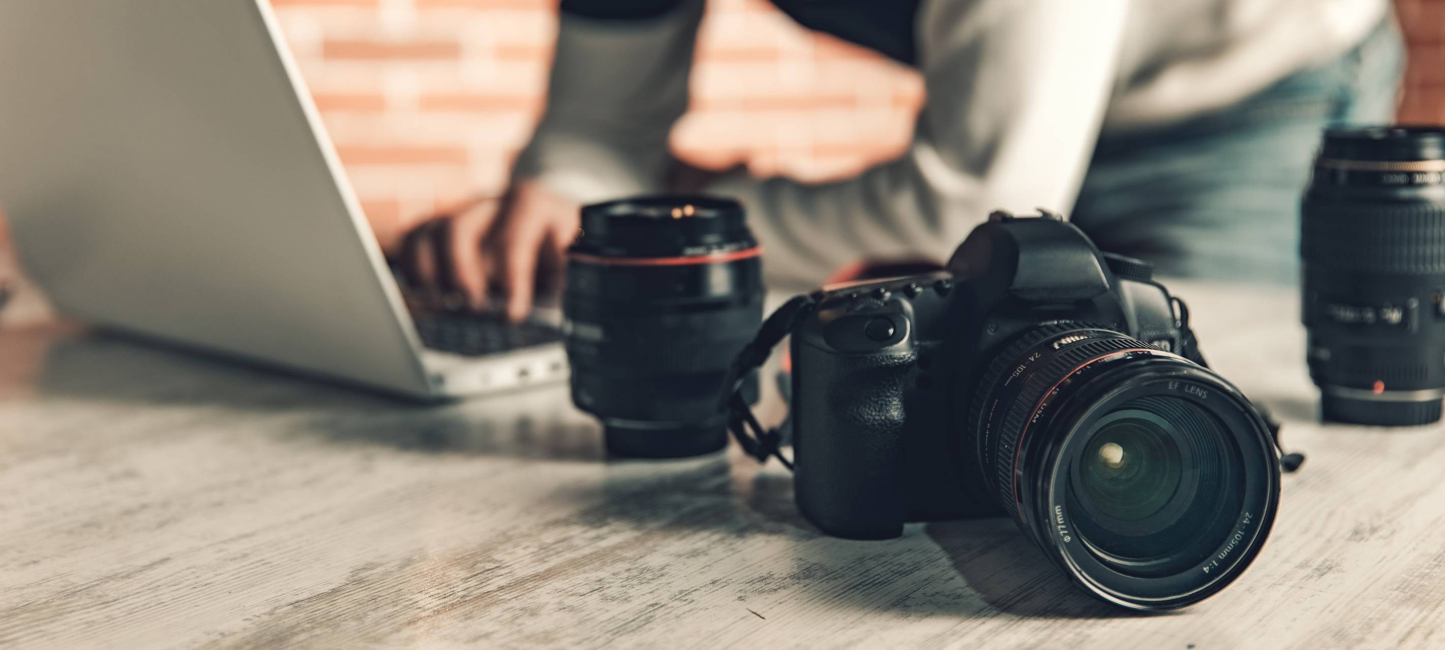 Nahaufnahme: Hand eines Fotografen an einer Kamera auf einem Schreibtisch.