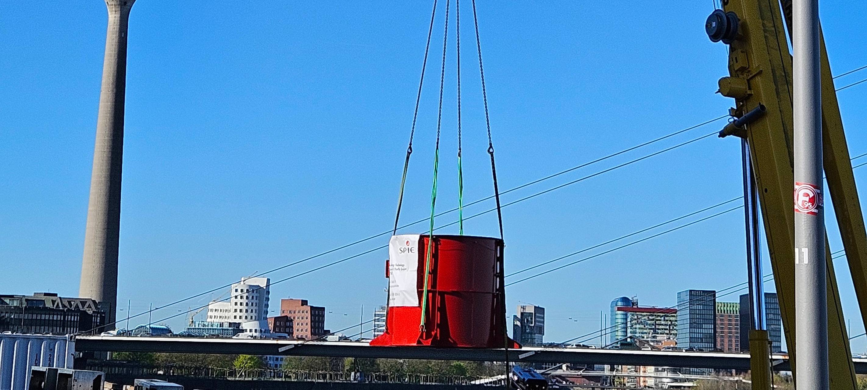 Teile eines Ventilators werden mit einem Kran in einen Schacht gehoben.