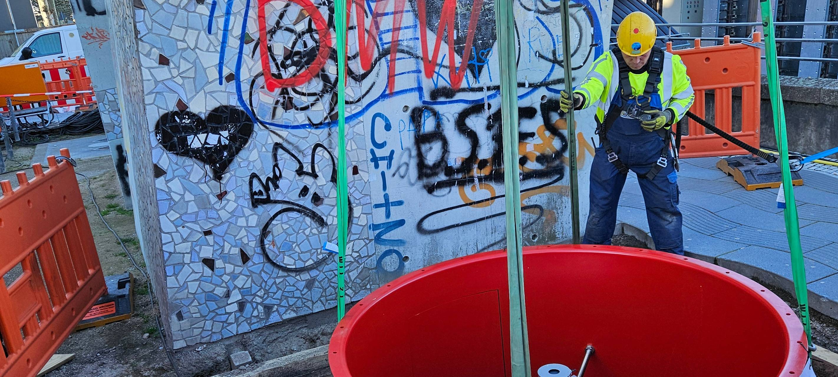 Teile eines Ventilators werden mit einem Kran in einen schmalen Schacht gehoben. Drumherum stehen Absperrzäune.