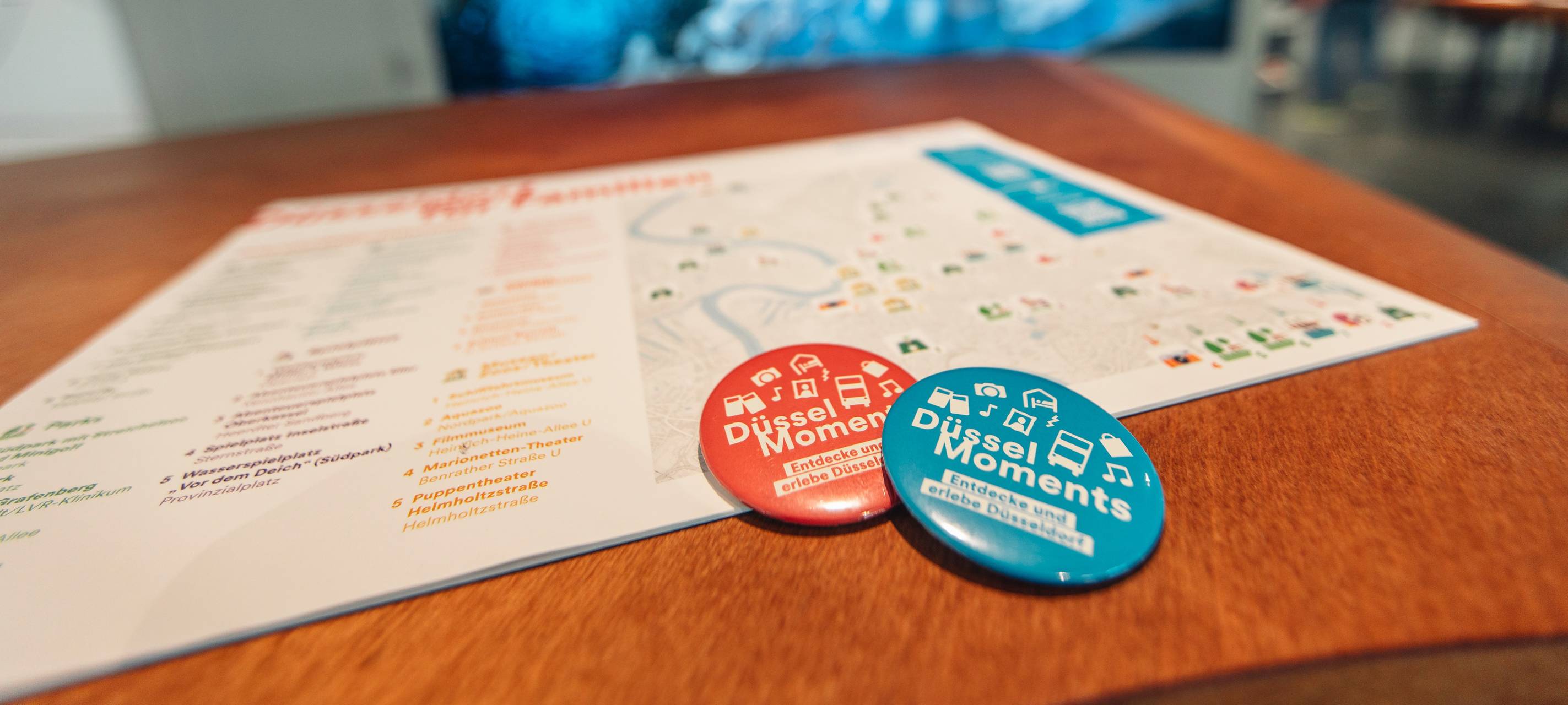 Ein Stadtplan zeigt die Highlights der DüsselMoments. Auf dem Plan liegen zwei Anstecker.