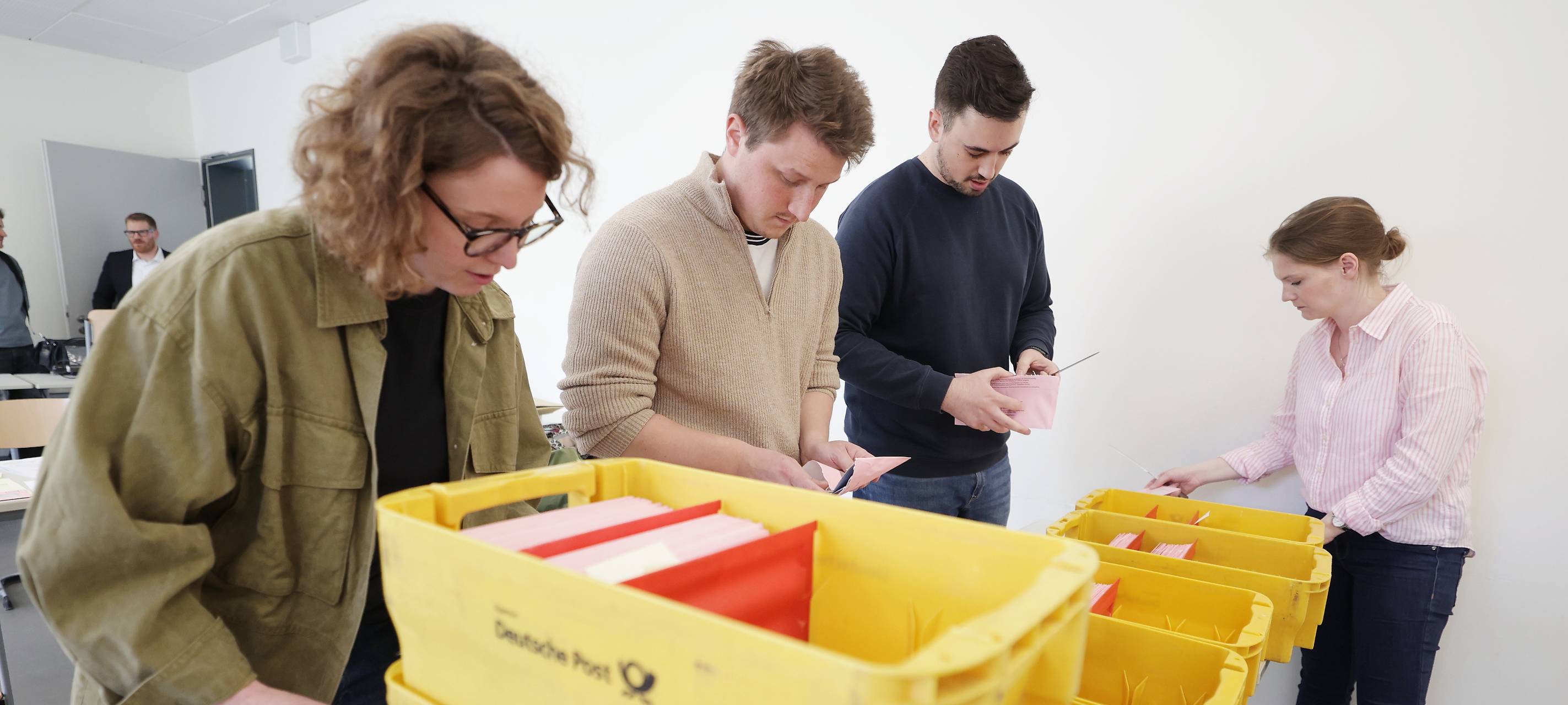 Mehrere Ehrenamtliche stehen neben vielen aufeinandergestapelten gelben Postkisten. Darin befinden sich die rund 155.000 Abstimmungsunterlagen aus Düsseldorf für den Olympia-Bürgerentscheid.