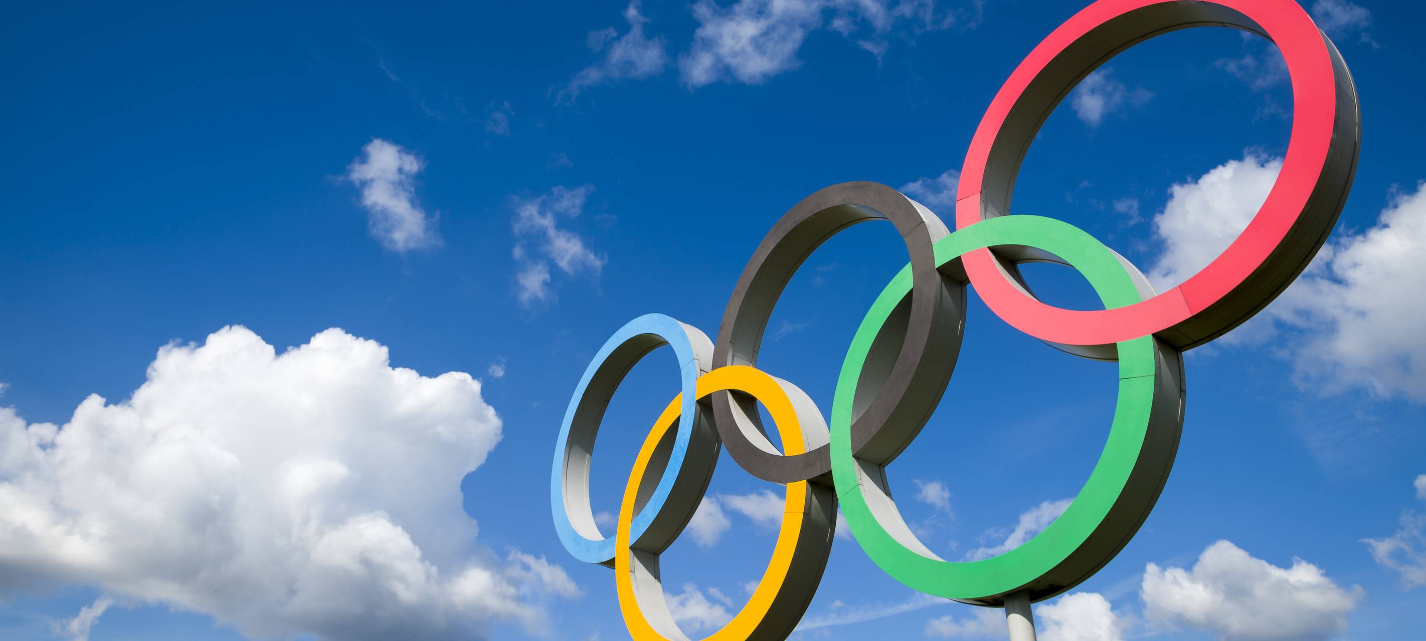 Die olympischen Ringe vor einem locker bewölkten, blauen Himmel