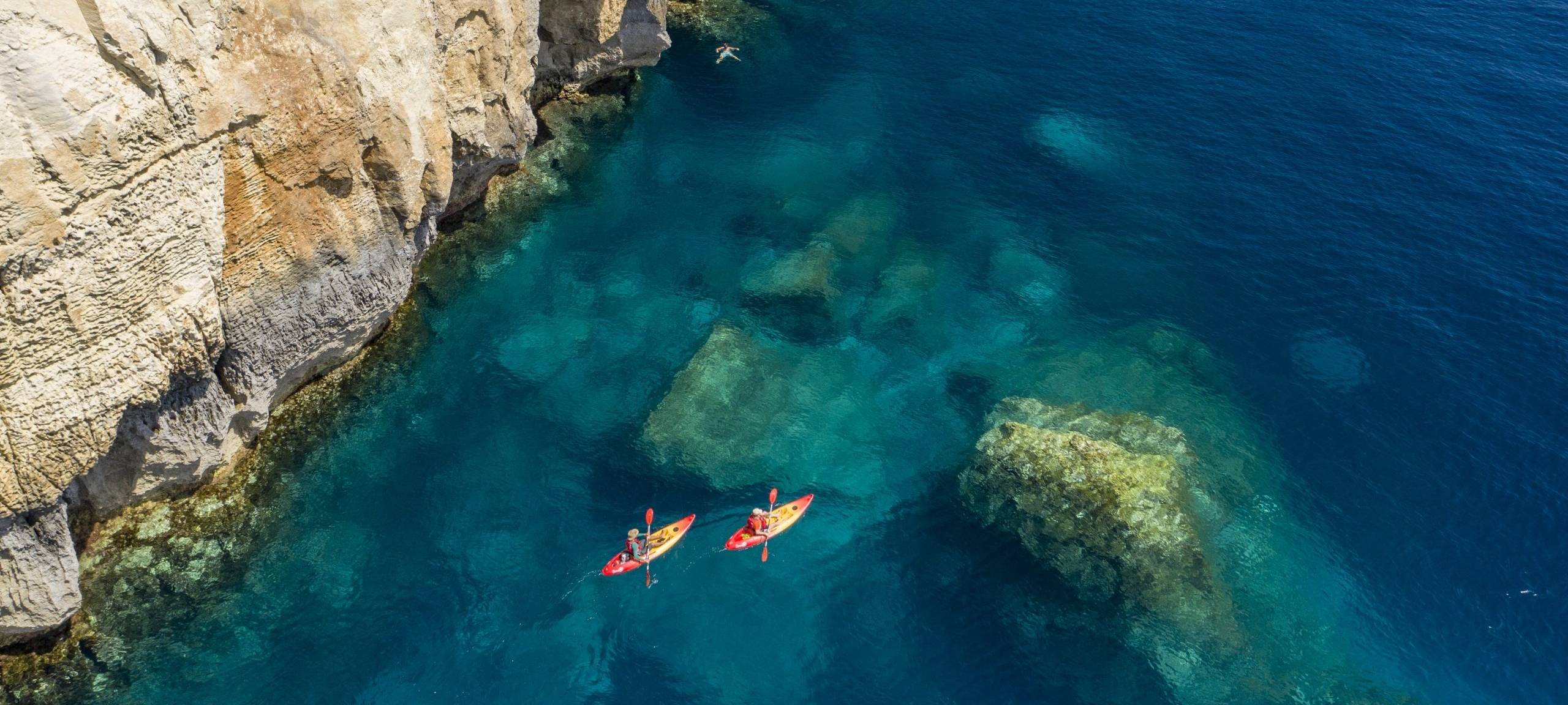 Eine Bucht vor Malta von oben. Man sieht das Meer, zwei Kanuboote und Klippen.