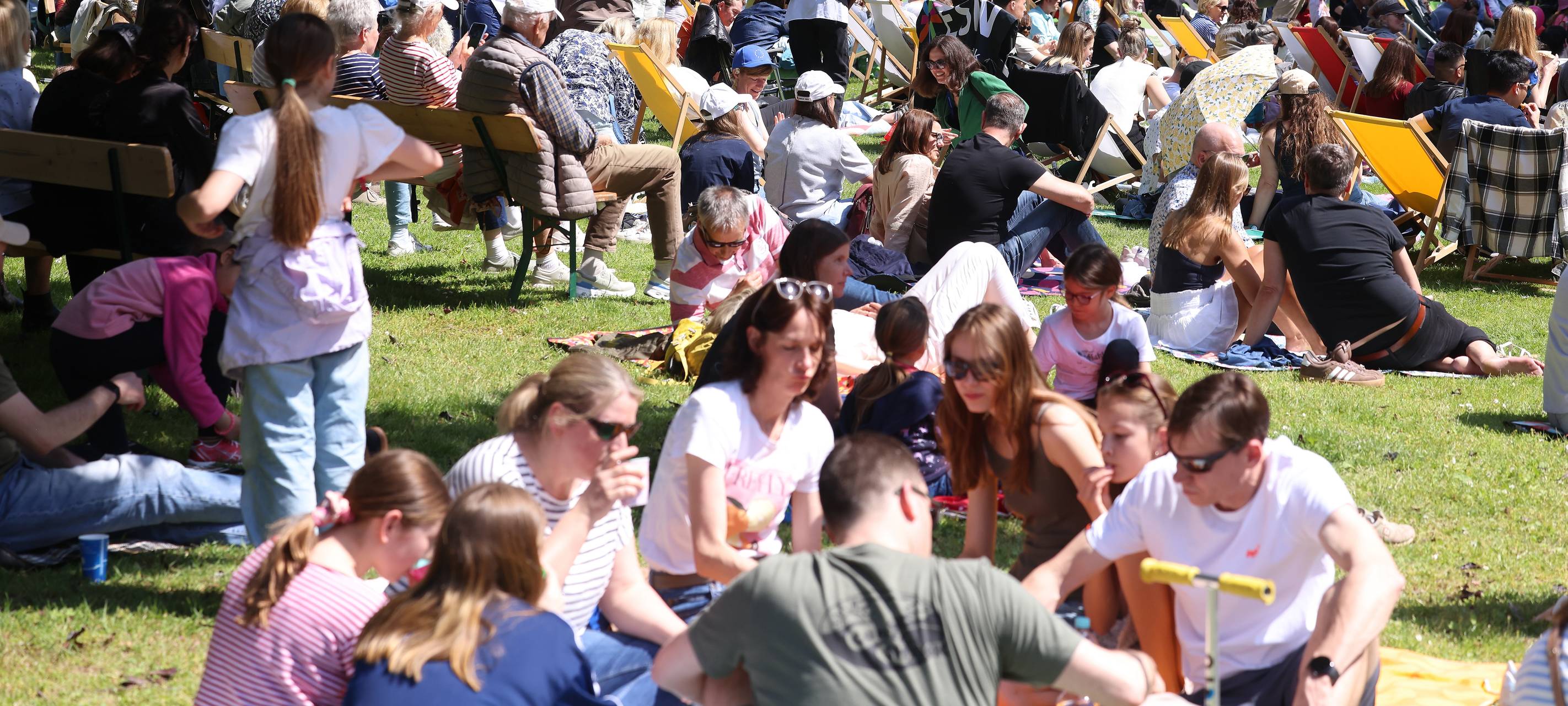 Menschen sitzen bei Sonnenschein im Park in Gruppen zusammen.