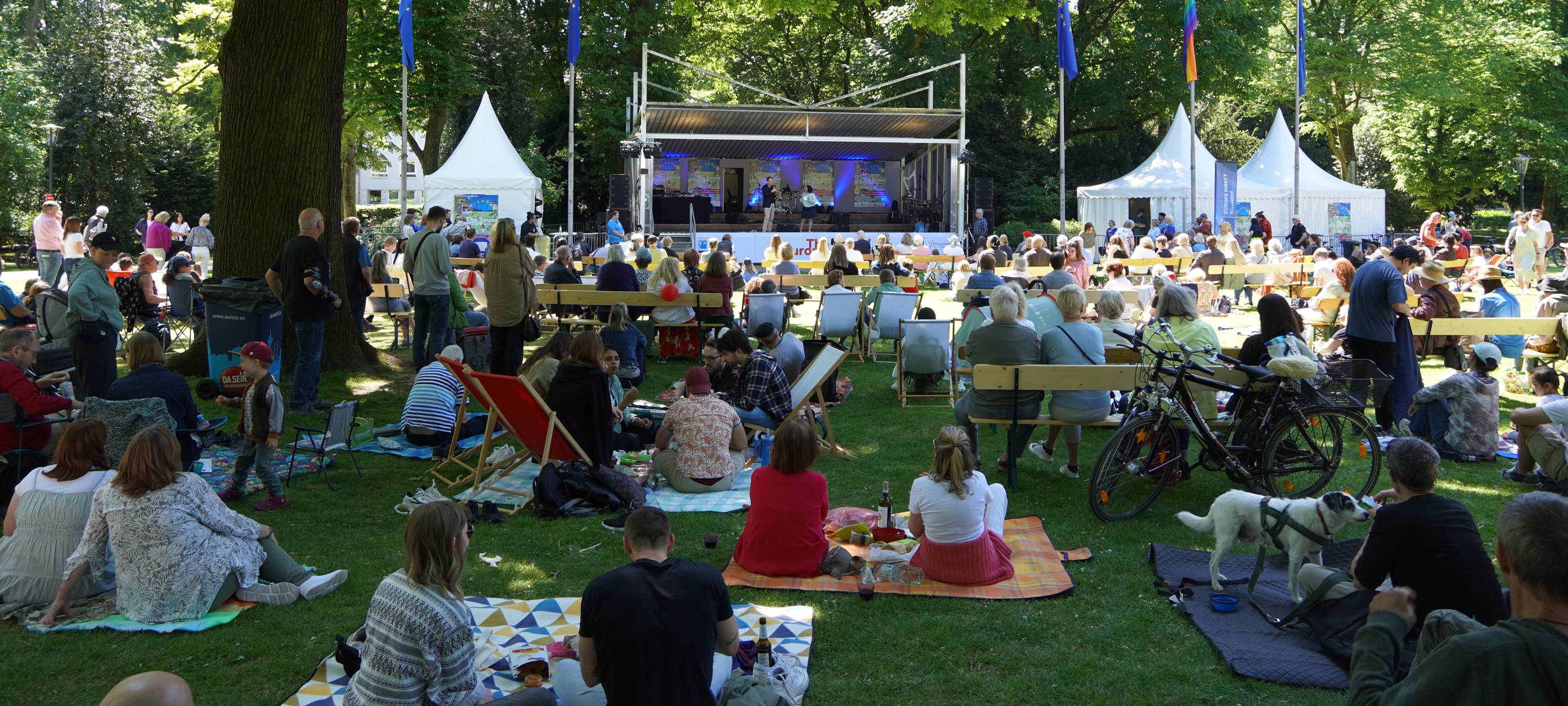Besucherinnen und Besucher sitzen beim Festival "The Sound of Europe" auf der Wiese vor der Bühne.