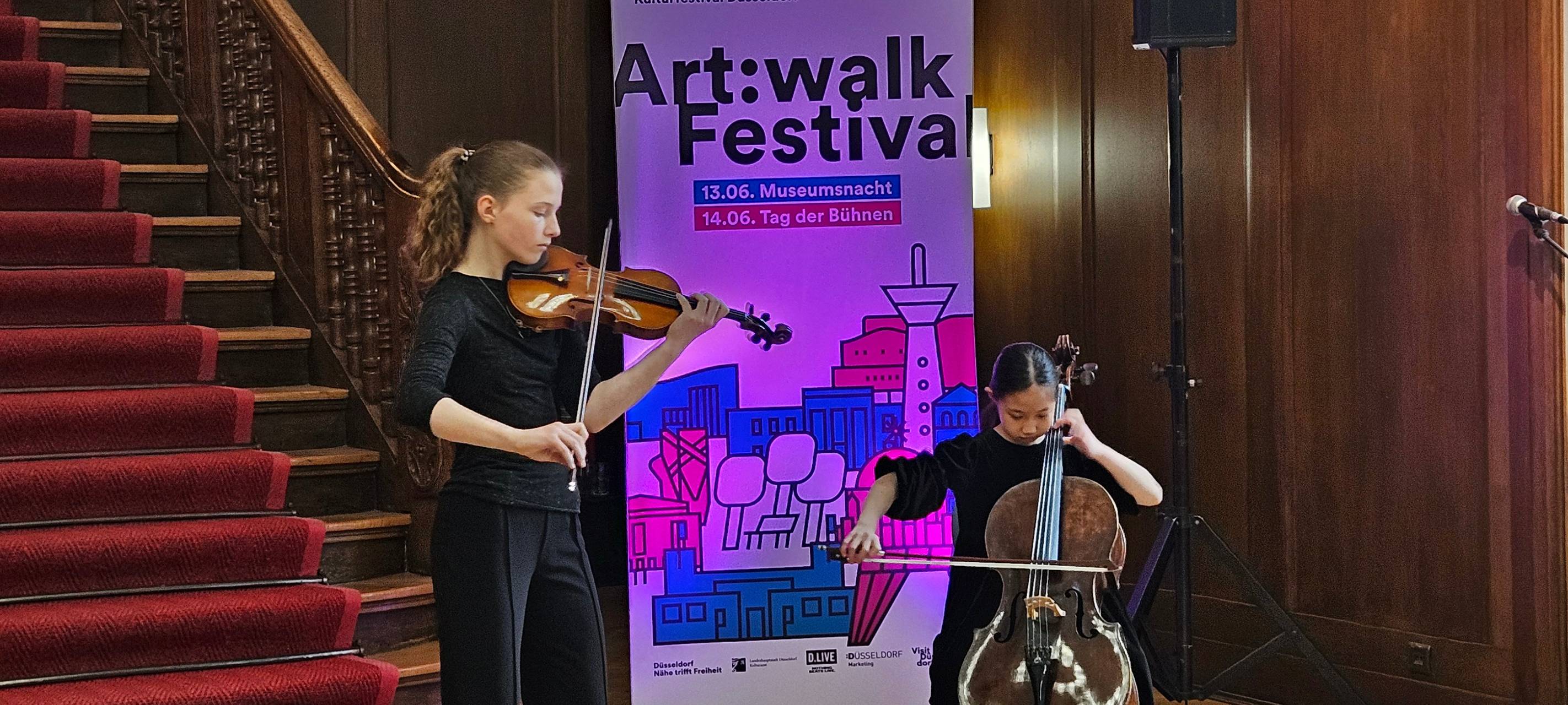 Schülerinnen der Clara Schumann Musikschule mit Cello und Geige vor einem Art:Walk festival Banner