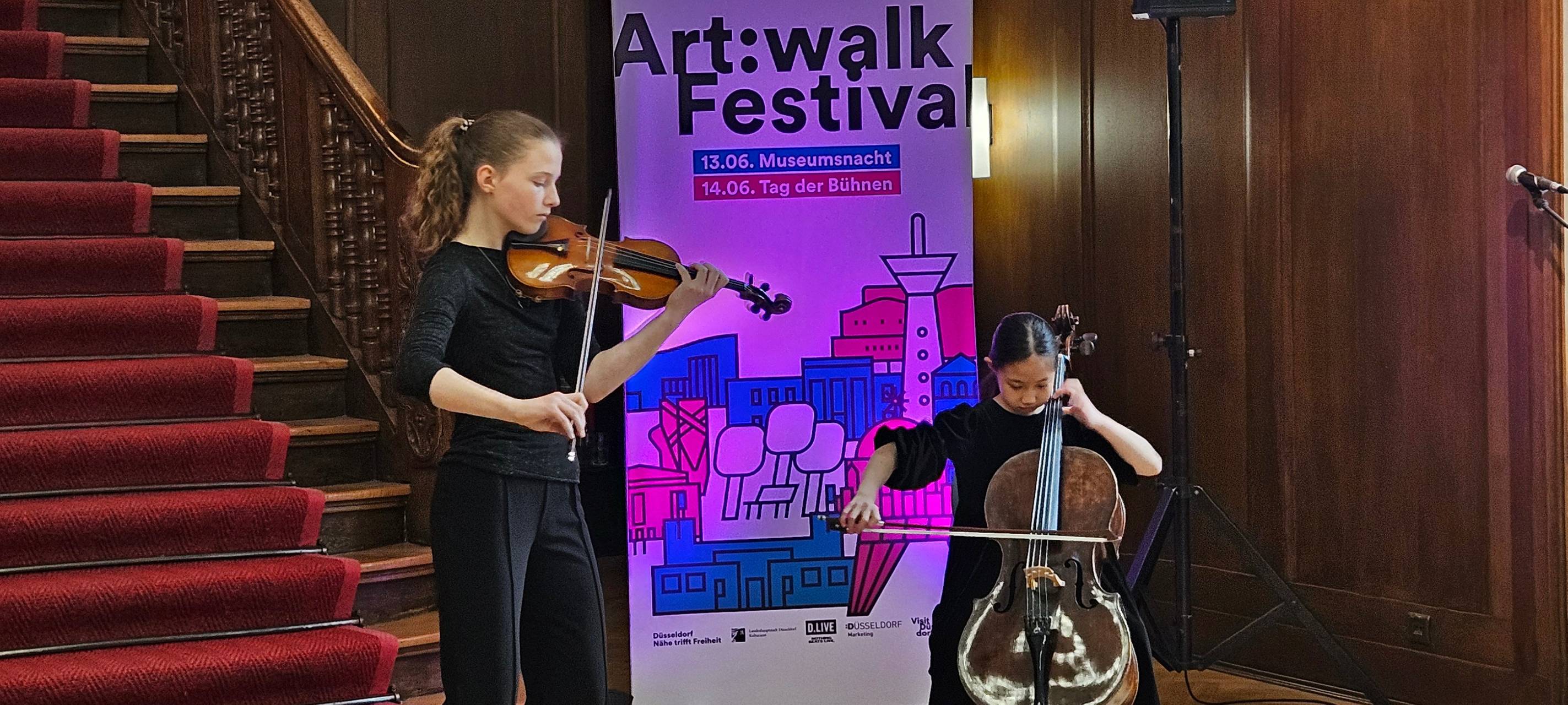Schülerinnen der Clara Schumann Musikschule mit Cello und Geige vor einem Art:Walk festival Banner