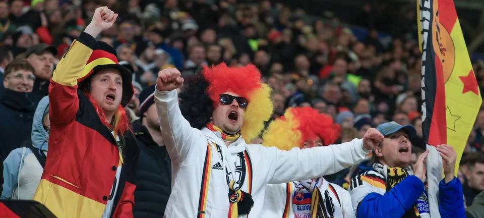 Bunt verkleidete Fans der deutschen Fußball-Nationalmannschaft jubeln in einem Stadion.
