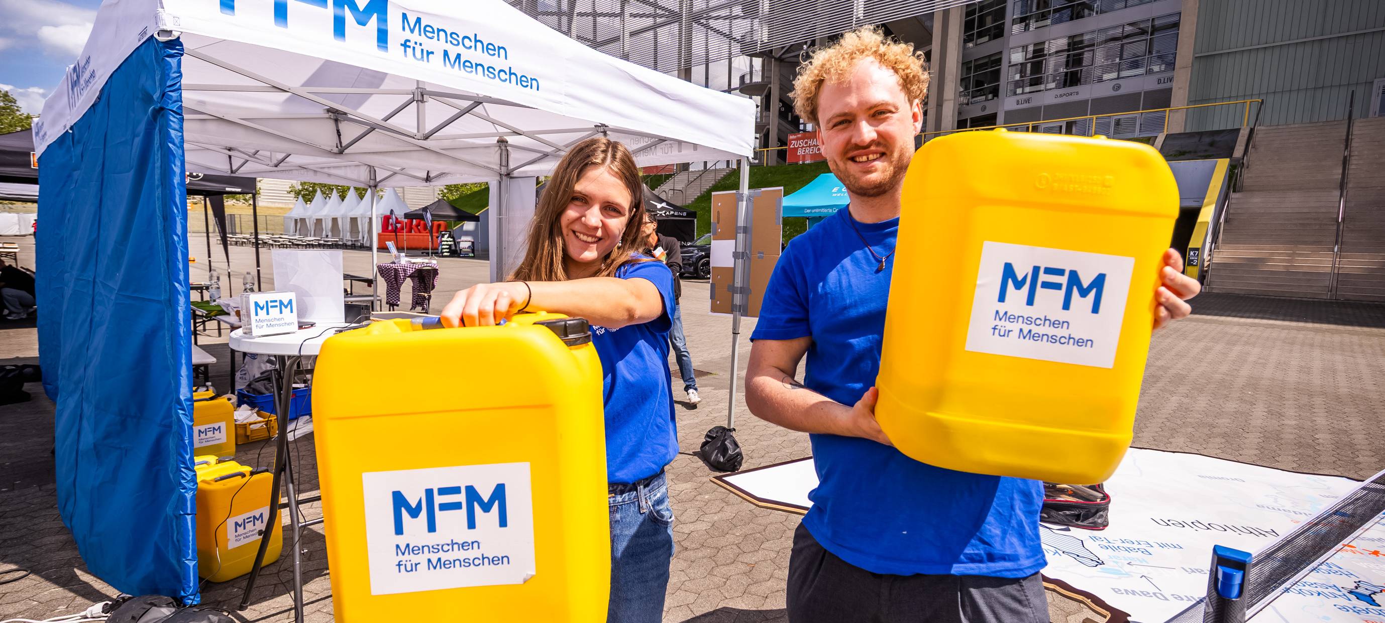 Zwei Mitglieder der Stifung "Menschen für Menschen" halten die gelben Wasserkanister der carry4water-challenge in die Kamera.