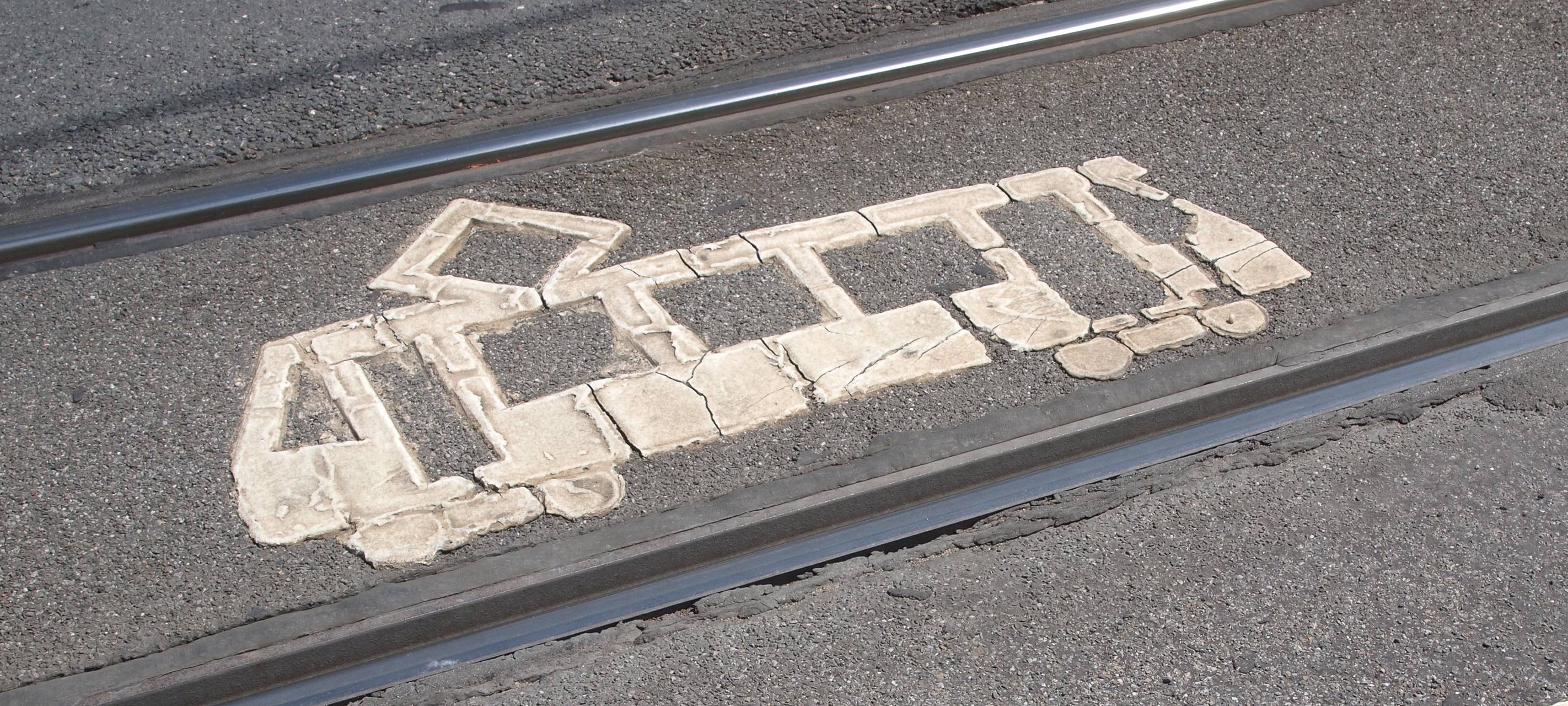 Die Silhouette einer Straßenbahn auf dem Asphalt zwischen zwei Straßenbahn-Gleisen.