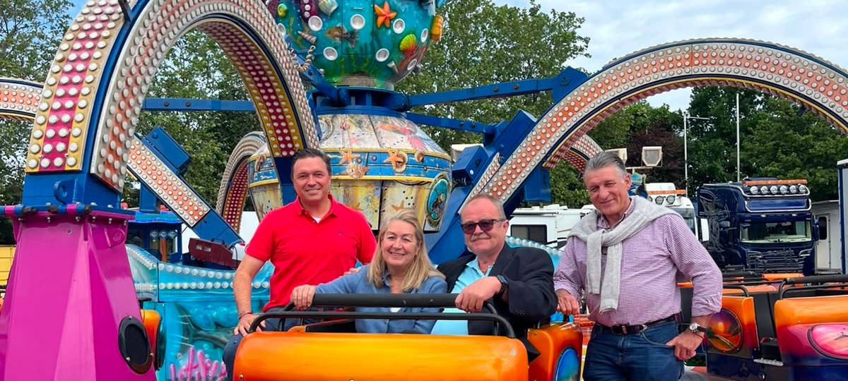 Ulrich Müller vom Schützenverein Bilk und eine Frau vom Schaustellerverband sitzen in einem Arm des Kirmes-Fahrgeschäfts "Krake". Daneben stehen Oliver Wilmering vom Schaustellerverband und ein weiterer Mann. Alle lächeln in die Kamera.