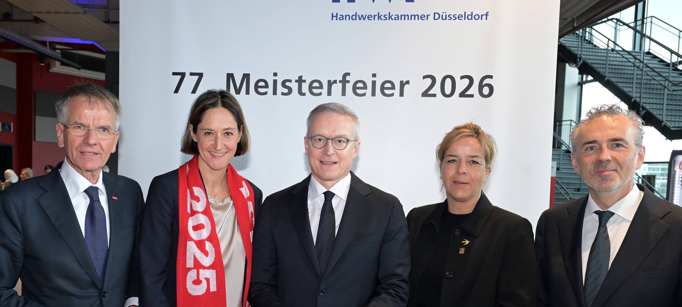 Präsident Andreas Ehlert, Jahresbestmeisterin Astrid Fedder, Bundesminister Dr. Karsten Wildberger, Landeswirtschaftsministerin Mona Neubaur und Staatssekretär Thomas Jarzombek MdB stehen vor einem Aufsteller mit dem Text "Meisterfeier 2026"