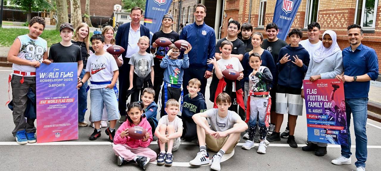 Verantwortliche der Stadt, der NFL und Schülerinnen und Schüler sind auf einem Gruppenfoto zu sehen. Die Schüler halten zum Teil Football-Eier in der Hand.