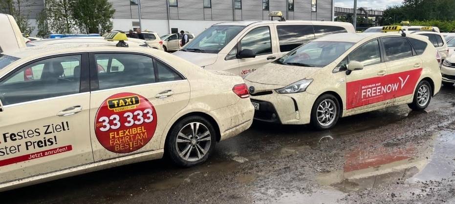 Das Bild zeigt Taxis auf dem Nachrückplatz am Flughafen. Die Straße ist schlammig und hat viele Pfützen