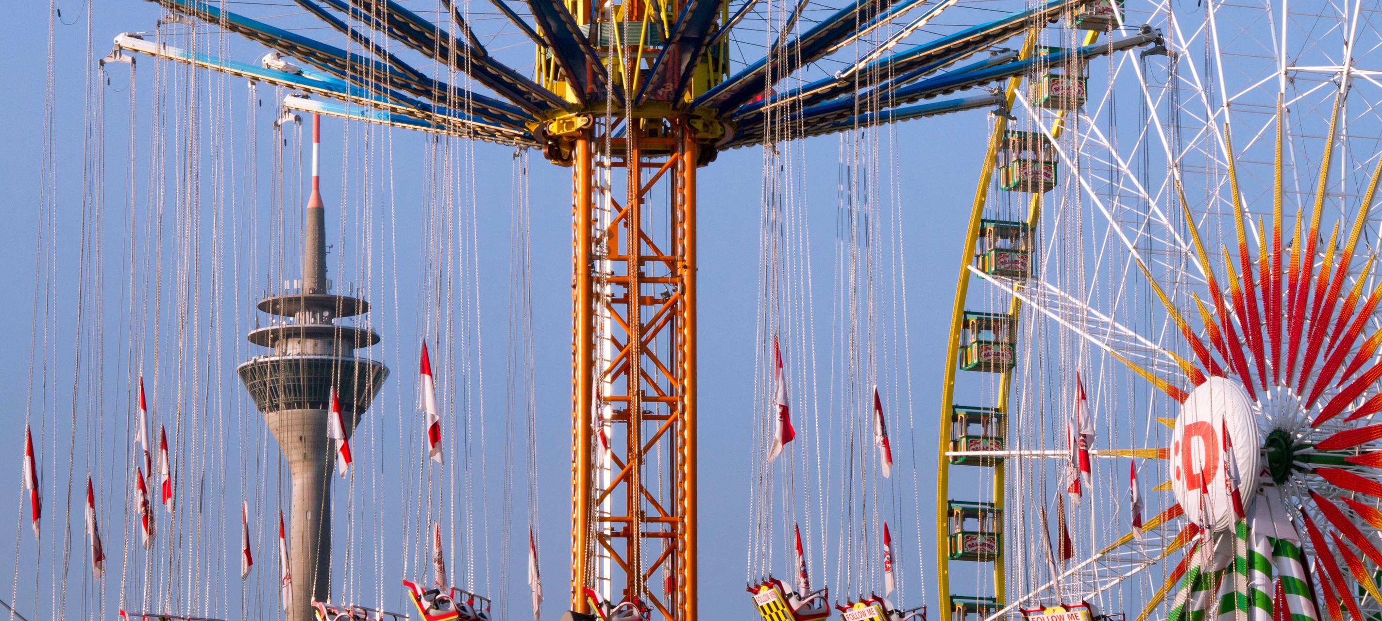Düsseldorfer Rheinkirmes 2026 mit Rheinturm, Riesenrad und weiteren Fahrgeschäften.