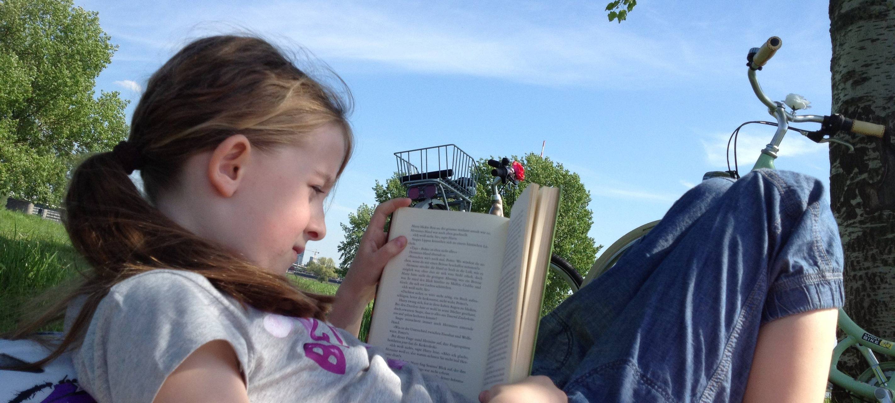 Ein Mädchen liest mit angewinkelten Knien auf einer Wiese und liest ein Buch
