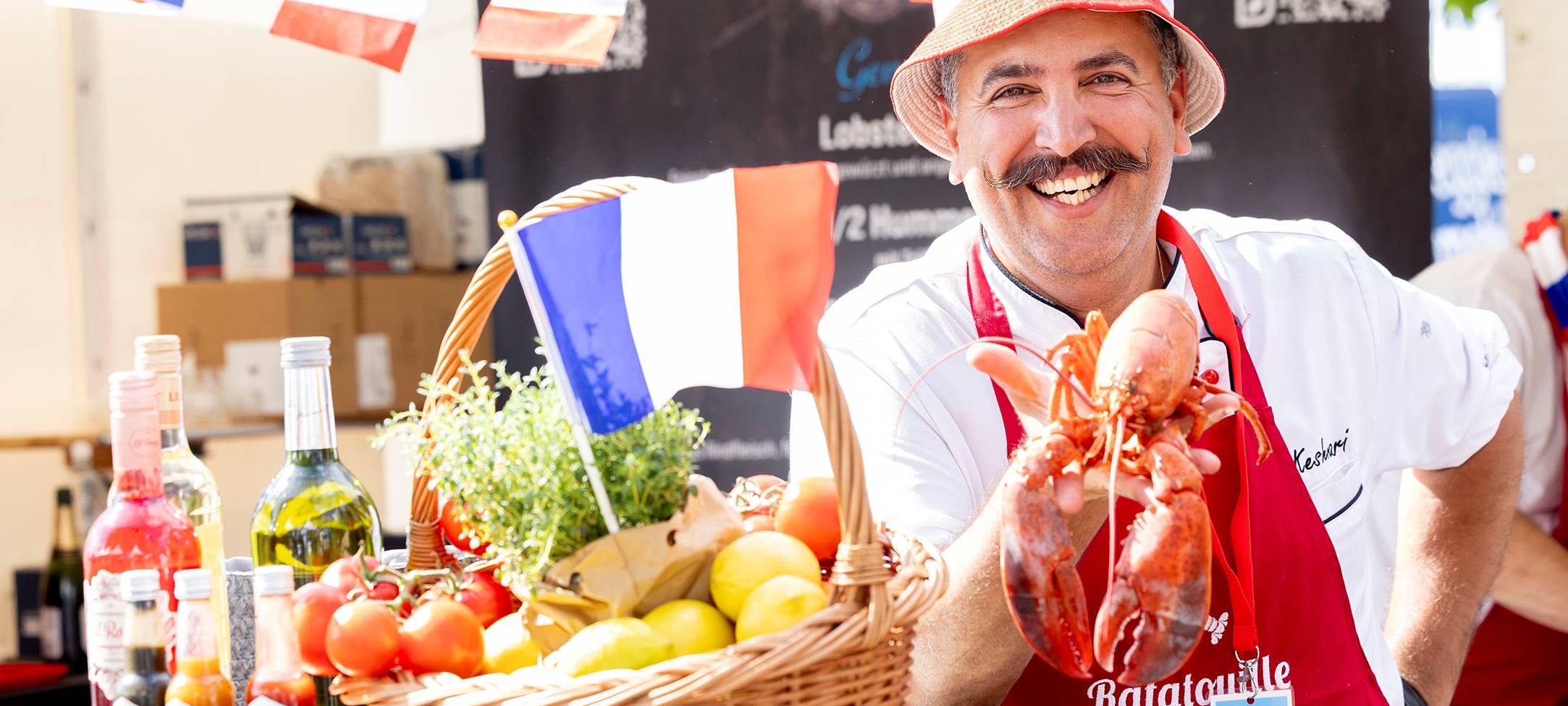 Ein Mann posiert mit Baguette, Käse, Trauben und Frankreichflaggen