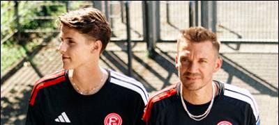 Zwei junge Männer tragen das schwarze Ausweichtrikot der Fortuna. Sie gehen eine Treppe hoch.