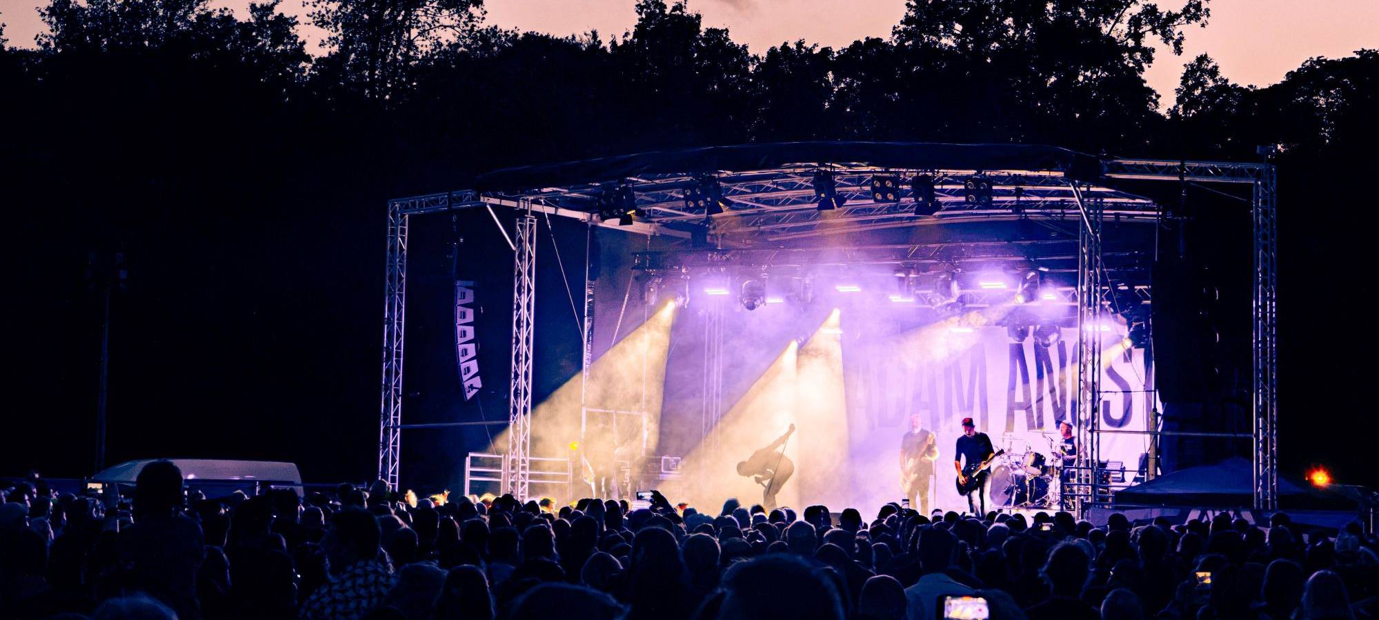 Ein Foto zeigt die Bühne von Rock gegen Rechts im Dunkeln. Vor der Bühne stehen viele Menschen. Die Bühne ist beleuchtet.