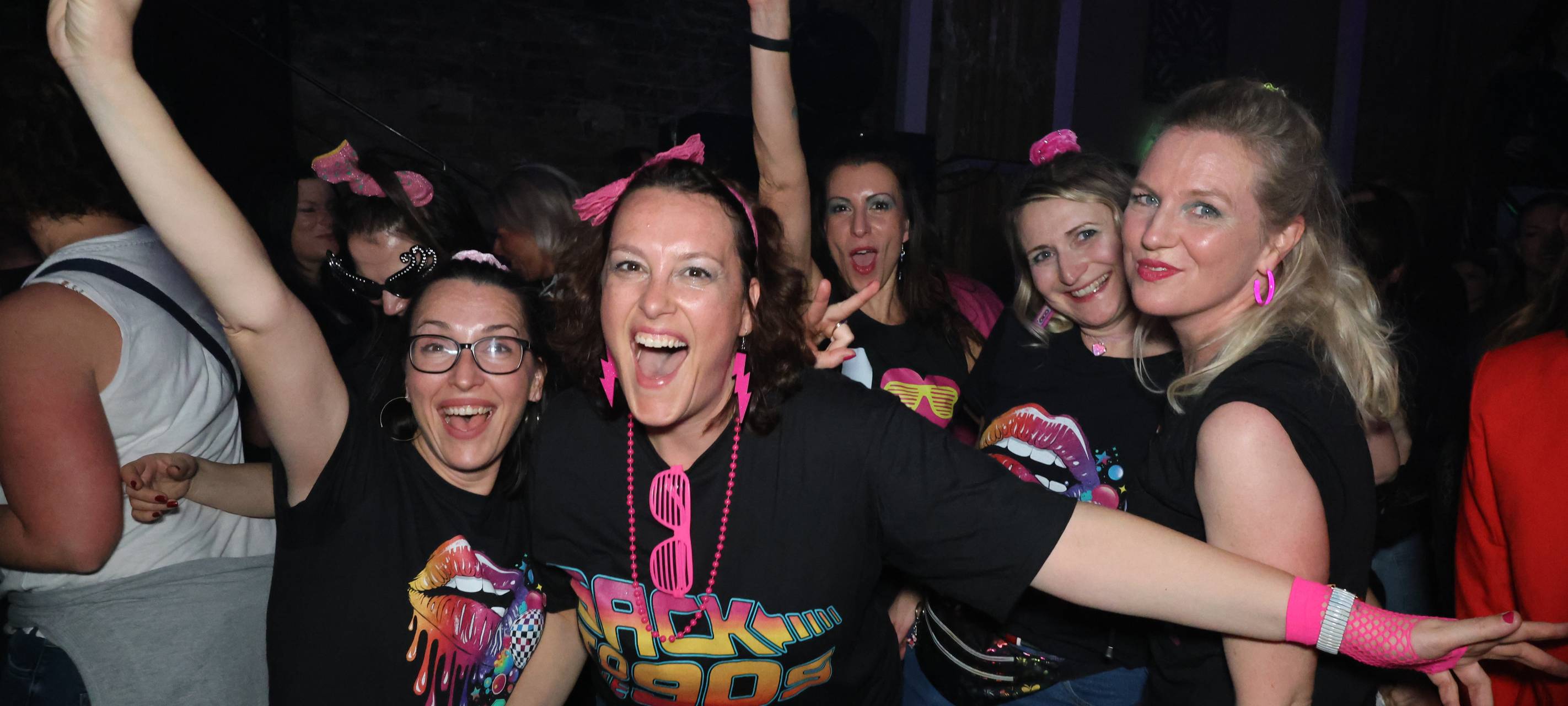 Mehrere gut gelaunte Frauen feiernd im 90er-Jahre-Look mit bunten Neon-Accessoires auf einer Party von Antenne Düsseldorf.
