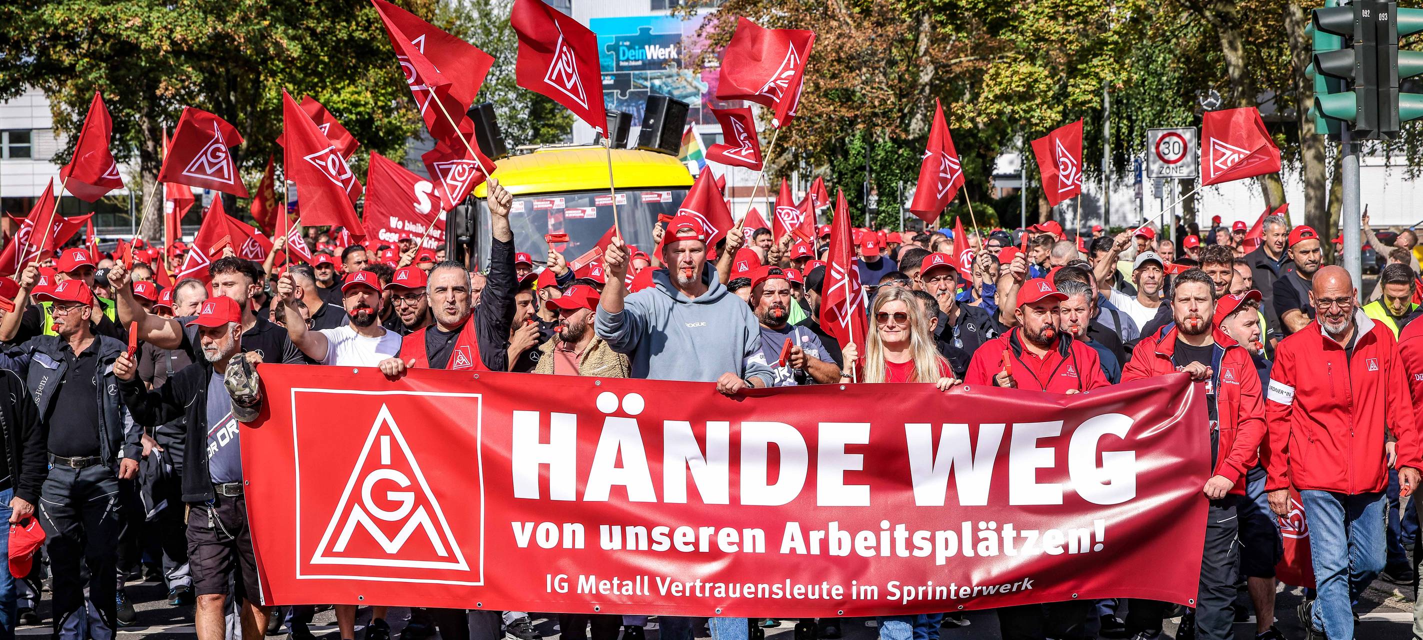 Demonstrierende der IG Metall laufen über eine Straße in Derendorf. Sie schwenken rote Fahnen und tragen ein Transparent mit der Aufschrift "Hände weg".