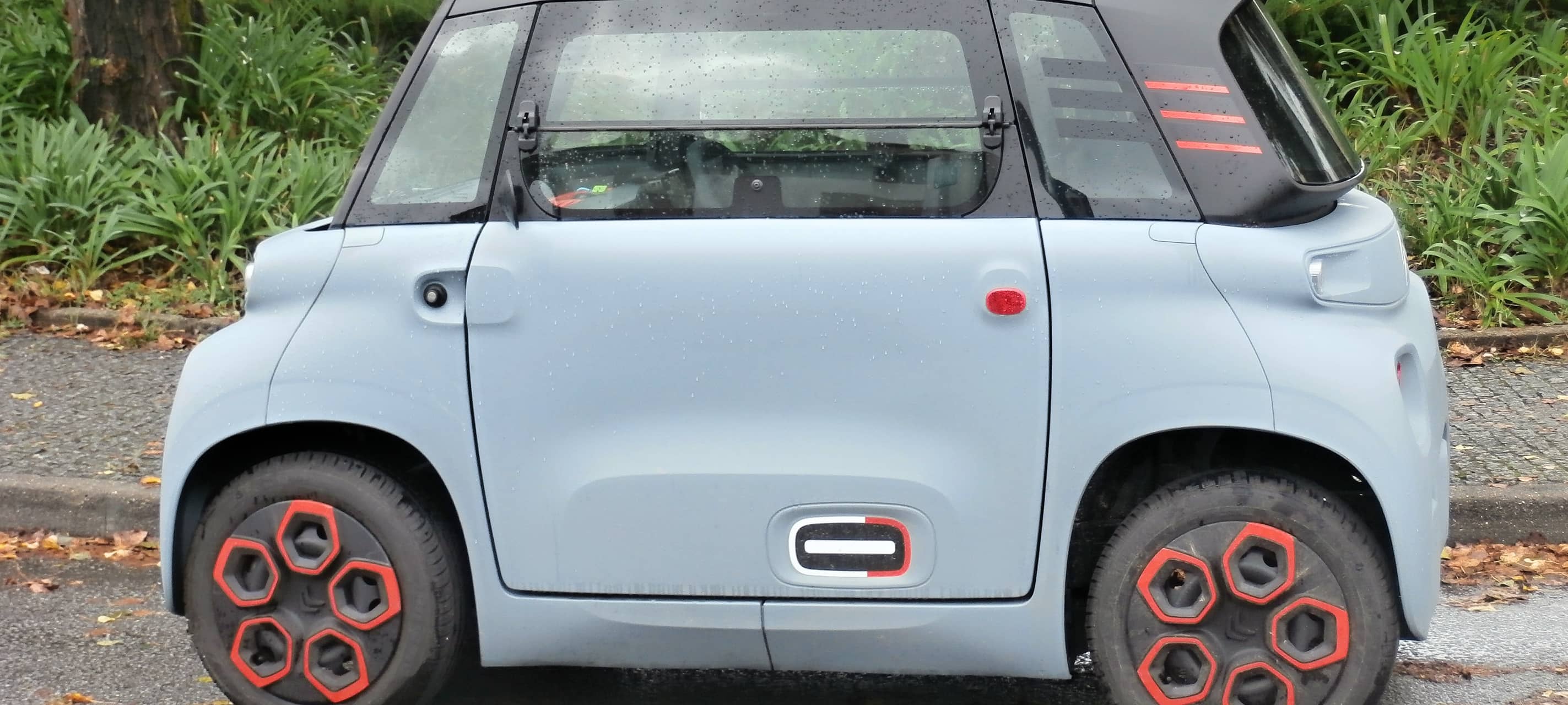 Ein graues Microcar, bzw. Mopedauto steht in einer Parklücke.
