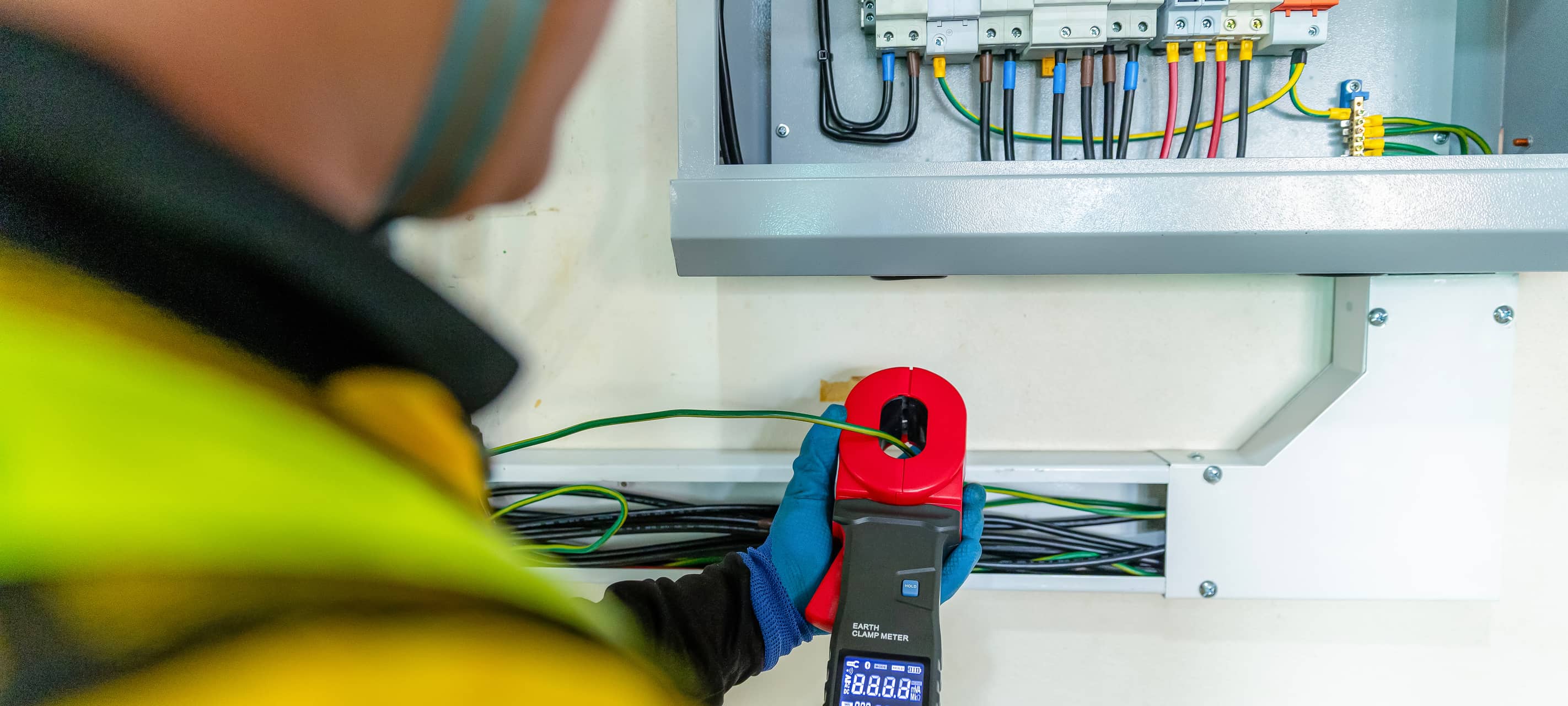 Elektriker prüft Verteilerkasten mit Zangenamperemeter - Symbol für Wartung am Düsseldorfer Stromnetz.