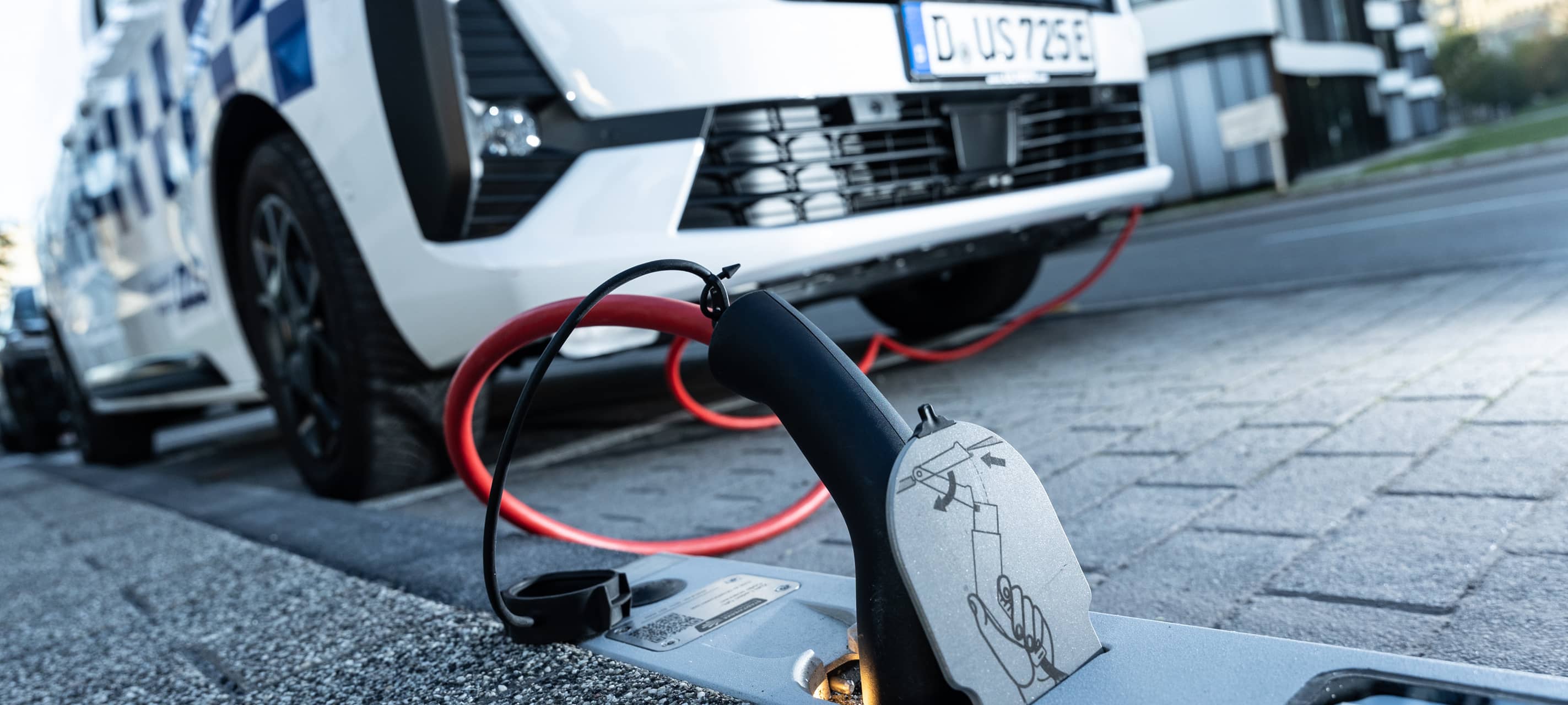 Ein E-Auto steht am Straßenrand und ist am Bordstein mit einem Kabel an eine Steckdose angeschlossen.