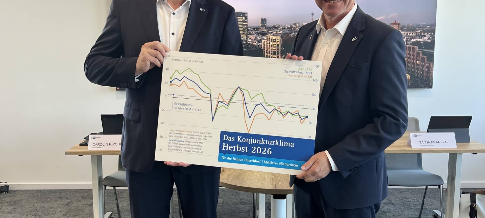 Gregor Berghausen (IHK Düsseldorf) und Jürgen Steinmetz (IHK Mittlerer Niederrhein) halten eine Grafik mit dem neuen Konjunkturbericht.