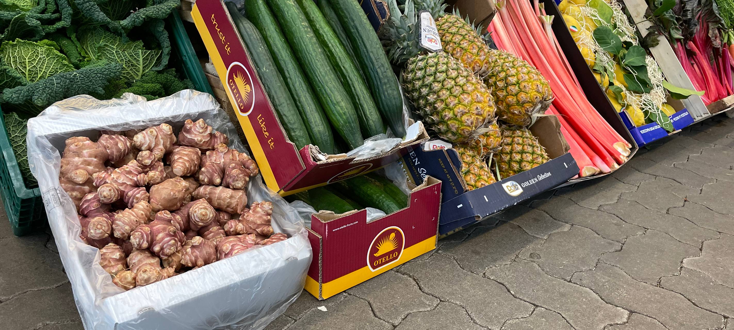 Verschiedene Obst- Gemüsekisten auf dem Großmarkt-Gelände. Unter anderem sind Gurken oder auch Äpfel zu sehen.