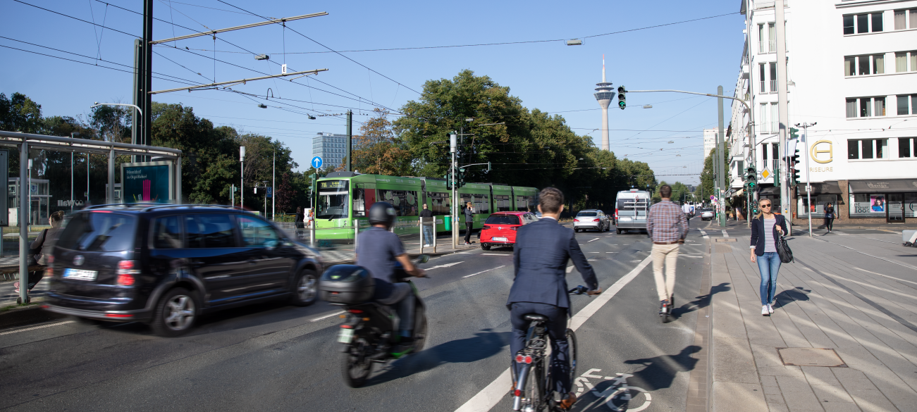 Symbolbild: Einige Verkehrsteilnehmer bewegen sich mit verschiedenen Verkehrsmitteln über eine Düsseldorfer Straße.