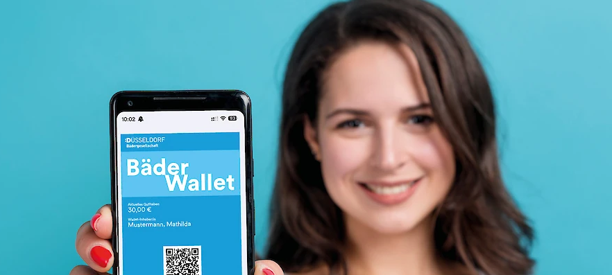 Eine Frau hält ihr Handy in die Kamera. Auf dem Bildschirm sind ein QR-Code und der Text "Bäder-Wallet".