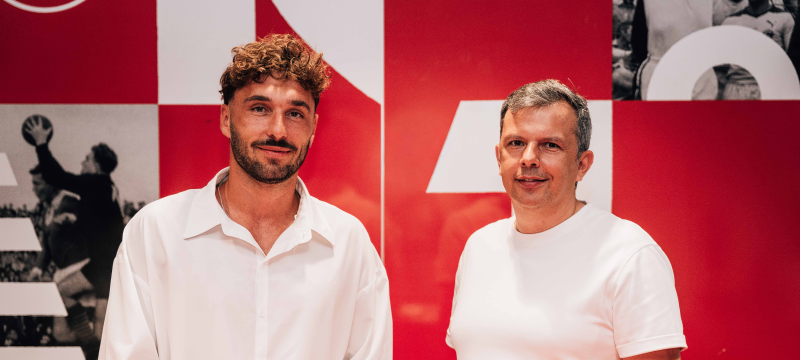 Fabian Schleusener und Sportvorstand Samir Arabi stehen vor einer roten Wand. Auf einer roten Theke liegt Risch' Vertrag. Er hält einen Stift in der Hand, beide lächeln.