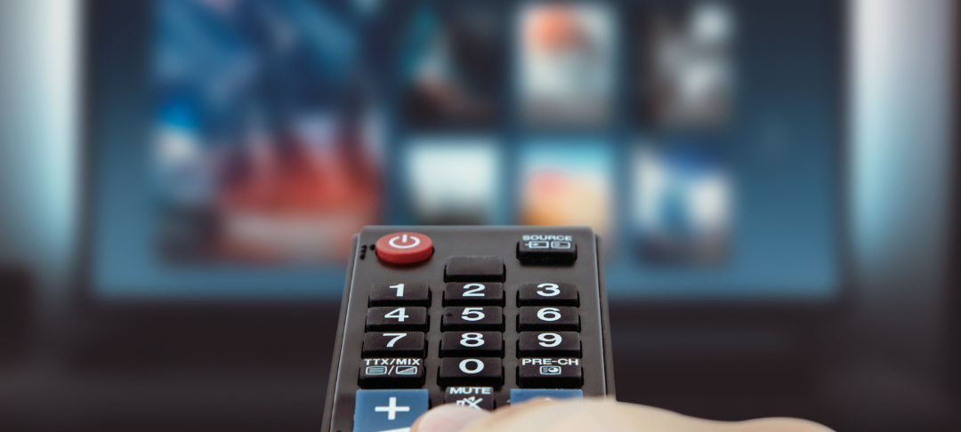 Fernbedinung zeigt auf TV im Hintergrund mit verschwommen zusehnenden Apps.