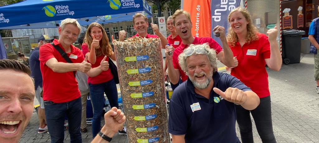 Das Team der Deutschen Postcode Lotterie vor einer Säule mit gesammelten Kippen in der Kippen-Woche.