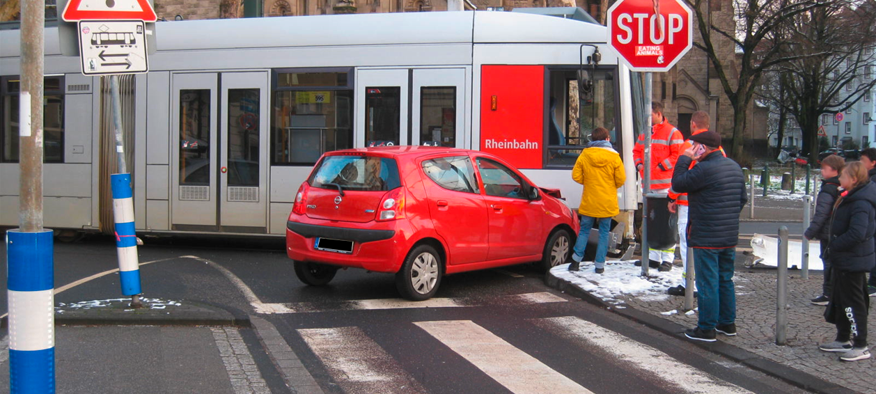 Ein rotes Auto und eine Straßenbahn sind auf einer Kreuzung ineinander gefahren.